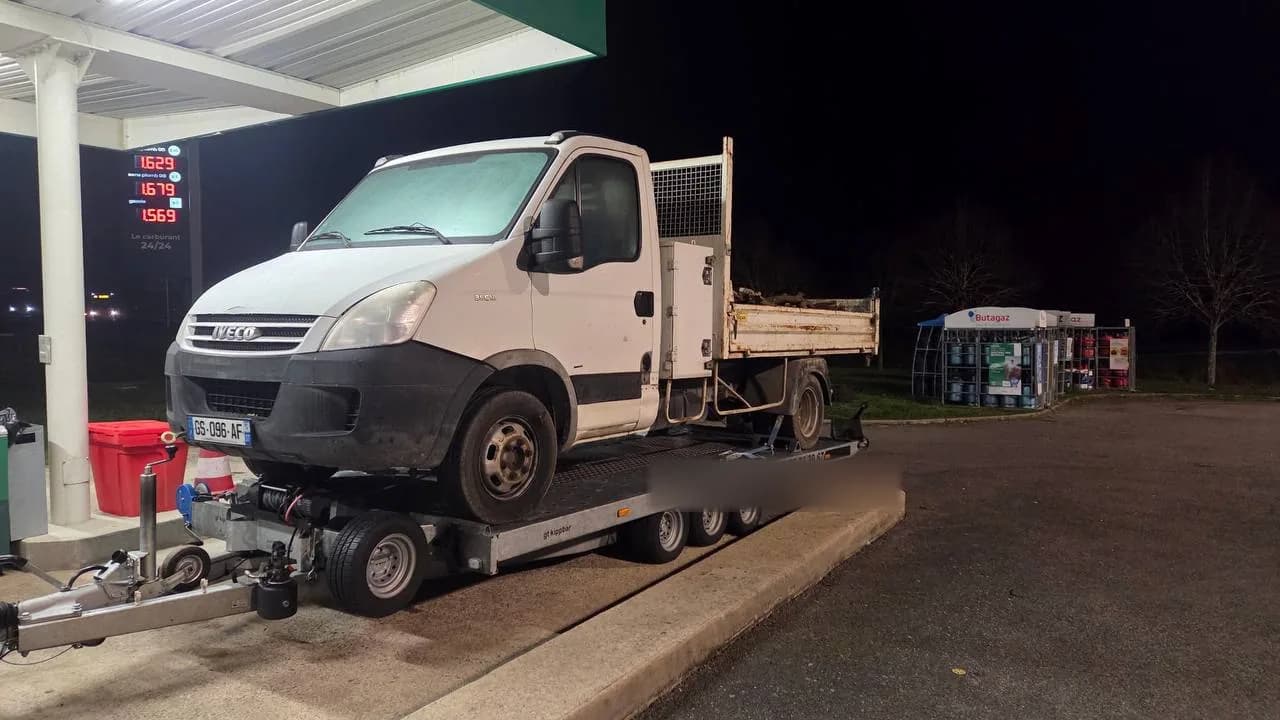 Camion benne Iveco Daily chargé sur remorque plateau de nuit sur une station-service lors d'un remorquage d'utilitaire