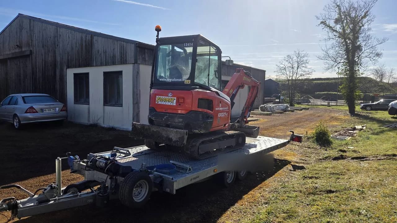Mini-pelle Kubota KX027-4 d'un loueur de matériel transportée sur remorque plateau vers un chantier