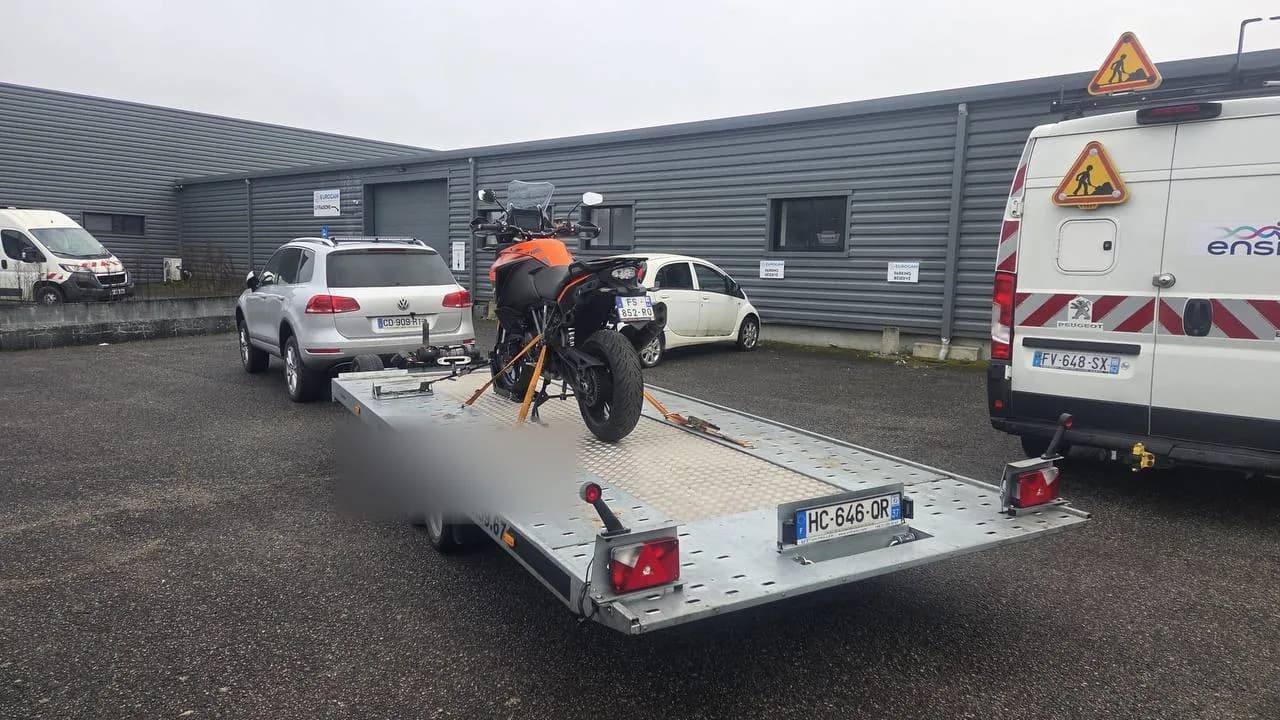 Moto KTM orange maintenue par bloque-roue et sangles sur remorque plateau lors d'un transport moto professionnel